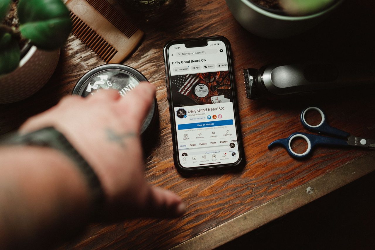 Barber tools and a smartphone showing a grooming brand site on a wooden table.